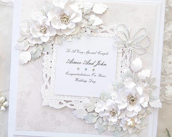 May include: White wedding card with a white lace frame and white flowers. The card reads "To A Very Special Couple Aimee And John Congratulations On Your Wedding Day".