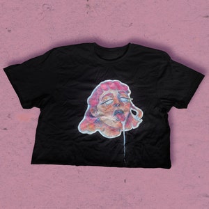 Può includere: Maglietta nera con una grafica di un viso di donna con capelli rosa e una sostanza che cola dalla sua bocca.