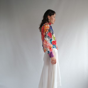 Op de afbeelding: Een vrouw draagt een kleurrijk patchwork shirt met een witte rok en witte cowboylaarzen.