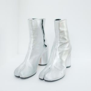 May include: A pair of silver leather ankle boots with a split toe design and a block heel.