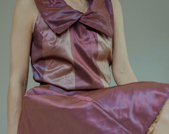 May include: A sleeveless dress with a large, folded collar. The dress is made of a shiny, iridescent fabric with vertical stripes in shades of pink, purple, and beige.