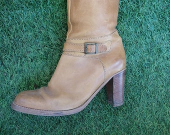 May include: Tan leather knee-high boots with a buckle strap and a block heel.