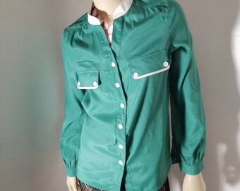 Peut inclure: Une chemise boutonnée à manches longues de couleur verte avec une bordure blanche autour du col et des poches. La chemise a un col mandarin et une fermeture à bouton unique au niveau du cou.