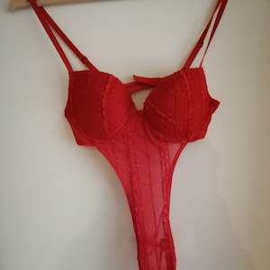 May include: Red lace lingerie with a plunging neckline and a sheer bodice. The lingerie has adjustable straps and a hook and eye closure at the back.
