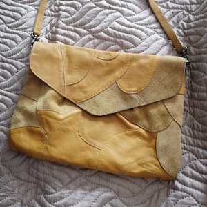 Peut inclure: Un sac à bandoulière en cuir jaune moutarde avec un design patchwork. Le sac a une fermeture à rabat et une longue bandoulière.