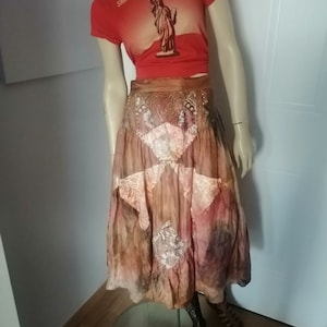 Peut inclure: Une jupe en patchwork marron et rose avec des détails brodés et un t-shirt rouge avec le texte "Smashing Pumpkins" et une image de la Statue de la Liberté.