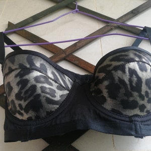 May include: A black strapless bra with a leopard print design. The bra has a silver metallic sheen and is made of a soft, stretchy fabric.