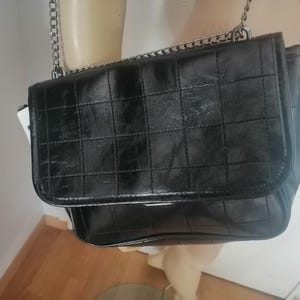 May include: A black, quilted shoulder bag with a silver chain strap. The bag has a rectangular shape with a flap closure. The bag is displayed on a mannequin.