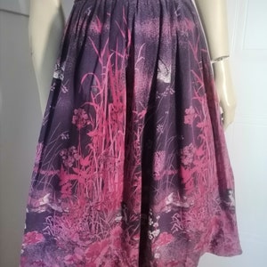 Peut inclure: Une jupe florale violette et rose avec une taille froncée. La jupe a un imprimé de fleurs et de feuilles roses sur un fond violet.