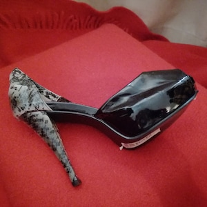 Könnte beinhalten: Schwarzer Plateau-High-Heel-Schuh mit Schlangenmuster an Ferse und Rücken. Der Schuh hat ein glänzendes Finish und einen Stiletto-Absatz. Der Schuh ist vor rotem Hintergrund platziert.