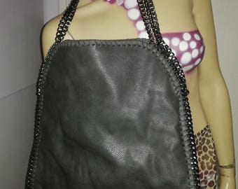 May include: A large, gray tote bag with a chain strap. The bag is made of a soft, textured material and has a chain trim around the edges. The chain strap is also gray. The bag is displayed on a mannequin.