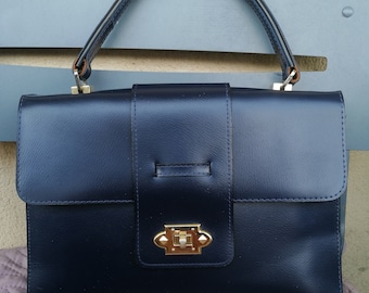 Könnte beinhalten: Eine dunkelblaue Ledertasche mit einem goldenen Verschluss und einem einzigen oberen Henkel.