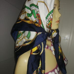 Peut inclure: Un foulard en soie avec une bordure bleu marine et un centre blanc orné d'une chaîne dorée et d'un motif de ventilateur vert. Le foulard est drapé sur une tête et des épaules de mannequin, mettant en valeur son motif et ses couleurs.