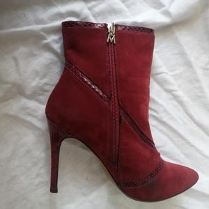 Op de afbeelding: Bordeaux enkellaars met een spitse neus en stilettohak. De laars heeft een zijrits en decoratieve afwerking. De hak en de afwerking hebben een slangenpatroon. De laars heeft een gouden ritstrekker.
