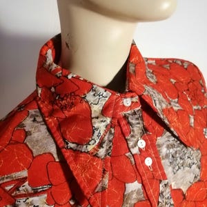 Peut inclure: Une chemise à boutons avec un motif floral audacieux en rouge, blanc et marron. Elle présente un col classique et des boutons blancs. Le tissu a un aspect texturé.