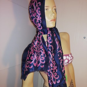 Peut inclure: Un foulard bleu marine avec un motif floral rose est drapé sur une tête de mannequin. Le foulard est fait d'une matière soyeuse et est noué autour du cou. Le mannequin porte une jupe léopard et un haut de bikini à pois.