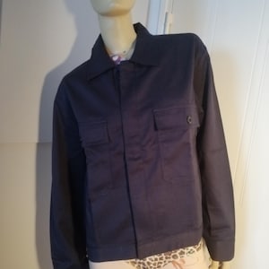 Peut inclure: Veste bleu marine avec deux poches poitrine et fermeture boutonnée, présentée sur un mannequin. La veste a un col et des manches longues. Le mannequin porte des sous-vêtements à motifs et des bas-cuisses.