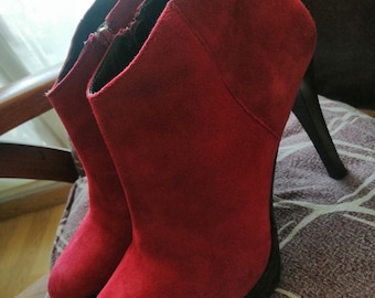 May include: A pair of red suede ankle boots with black heels. The boots have a pointed toe and a zipper on the inside of the ankle.