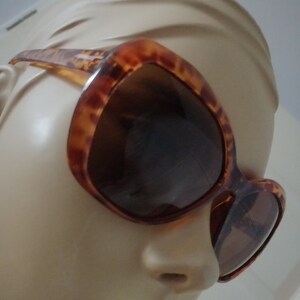 Peut inclure: Lunettes de soleil en écaille de tortue avec des verres bruns. Les lunettes sont sur une tête de mannequin.