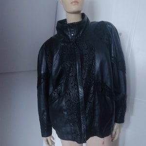May include: Black leather jacket with a high collar and a textured snake-skin pattern on the shoulders and front. The jacket has a zipper closure and long sleeves. A classic outerwear piece.