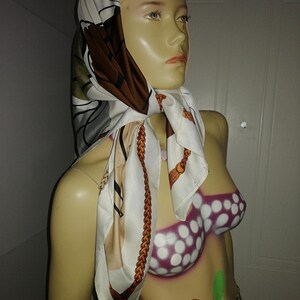 May include: A silk scarf with a brown, white, and gray pattern is draped around a mannequin's neck. The scarf features a chain design and is paired with a leopard print skirt. The mannequin has a painted bikini top.