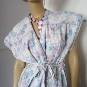 Peut inclure: Une robe blanche à imprimé floral dans les tons bleus et violets. La robe a une ceinture à la taille et des manches courtes avec une bordure à volants.