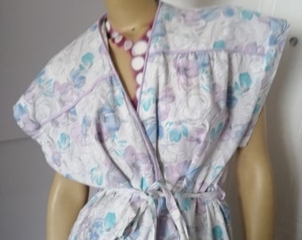 May include: A white robe with a floral print in shades of blue and purple. The robe has a tie at the waist and short sleeves with a ruffled trim.