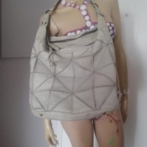 Peut inclure: Un sac à bandoulière beige clair avec un motif géométrique. Le sac a une grande capacité, une fermeture éclair et une longue bandoulière. Le sac est fait d'un matériau souple et a un aspect texturé unique.