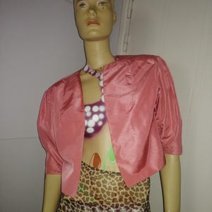 May include: A pink cropped jacket with a slightly puffed sleeve. The jacket is made of a silky material and has a simple design.