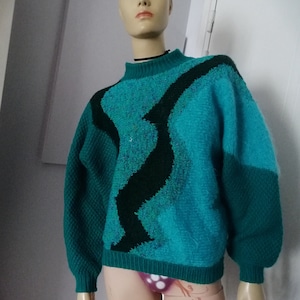 Puede incluir: Un suéter de color turquesa y negro con cuello alto. El suéter está hecho de un material suave y peludo.
