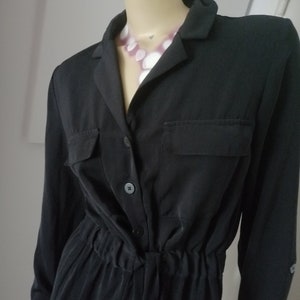 Peut inclure: Une robe noire à manches longues boutonnée avec un col et deux poches. La robe a une taille à cordon et une coupe ample.