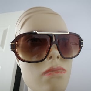 Peut inclure: Lunettes de soleil aviateur brunes avec une monture en métal doré et des verres teintés bruns.