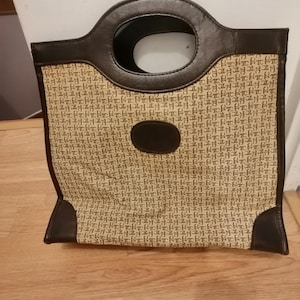 Peut inclure: Un sac fourre-tout marron et beige avec une poignée circulaire. Le sac présente un motif répété d'une lettre stylisée "H" en beige sur un fond beige. La poignée et la garniture sont de couleur marron foncé.
