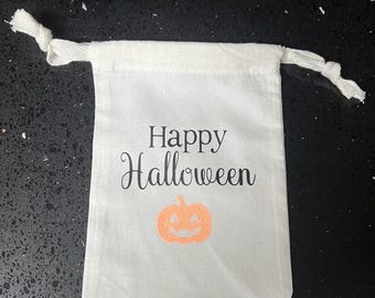 May include: White cotton drawstring bag with the text "Happy Halloween" and a small orange pumpkin with a smiling face.