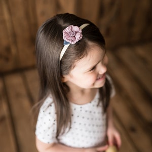 Pu&ograve; includere: Una bambina con lunghi capelli castani che indossa una camicia bianca a pois e una fascia per capelli con un fiore rosa.