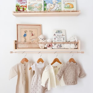 May include: A display of children's items, including books, framed art, and clothing. The books on the shelves have titles like "I Love You, Funny B" and "Guess How Much I Love You." The clothing includes a romper, sweater, and cardigan.