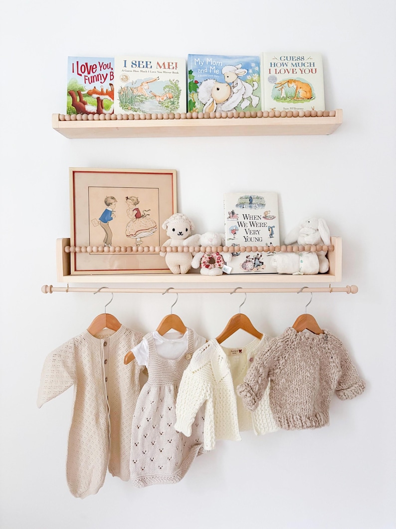 May include: A display of children's items, including books, framed art, and clothing. The books on the shelves have titles like "I Love You, Funny B" and "Guess How Much I Love You." The clothing includes a romper, sweater, and cardigan.