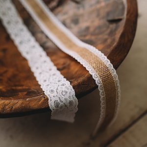May include: Two decorative ribbons rest in a wooden bowl. One is white lace, the other is burlap with a white lace trim. The ribbons are ideal for crafts, weddings, or home decor projects.