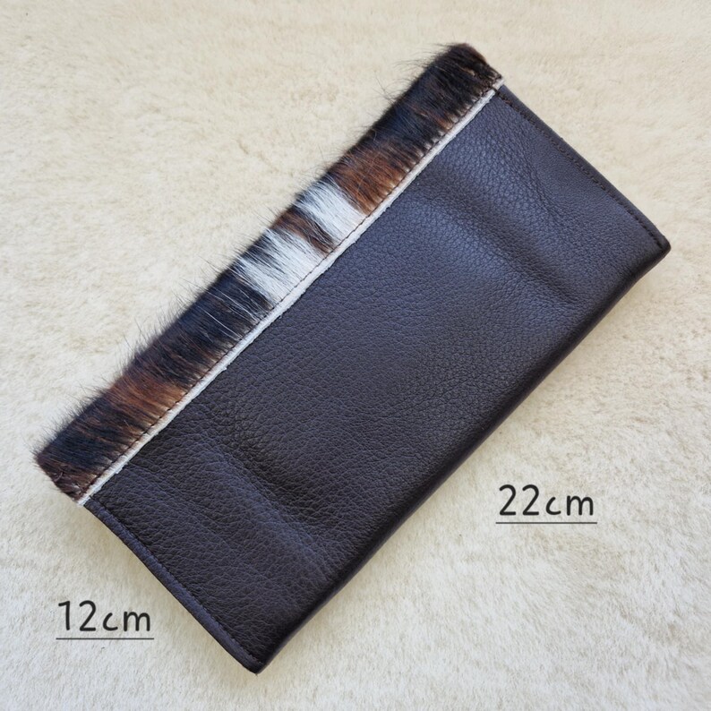 May include: A dark brown leather wallet with a section of cowhide hair in shades of brown, black, and white. The wallet measures 4.7 inches wide and 8.7 inches long.