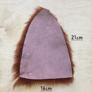 May include: A brown faux fur ear shape with a pink suede interior. The ear measures 16 cm wide and 21 cm tall. The item is likely for a costume or craft project.