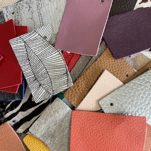 May include: A collection of leather and fabric swatches in various colors and textures. Includes samples in shades of pink, orange, brown, gray, and black. Some swatches have a pebbled texture, while others feature patterns like zebra stripes and a black and white leaf design.