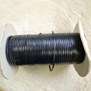 May include: A black leather cord wound on a cardboard spool. The cord is tightly packed, with a smooth, flat appearance. The spool has white edges. Ideal for crafts or jewellery making.