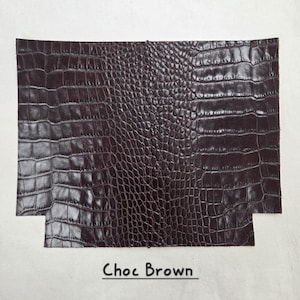 May include: A rectangular piece of dark brown leather with a crocodile skin texture. The leather has a glossy finish and is labeled "Choc Brown" in a handwritten font.