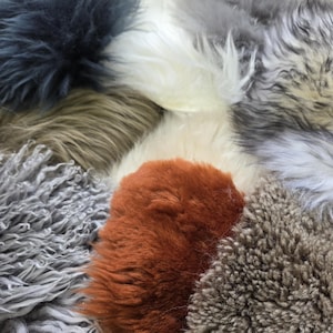 May include: A close-up view of various textured faux fur fabrics in a variety of colors. The colors include shades of gray, white, brown, and orange. The fur appears soft and fluffy, with varying lengths and textures.