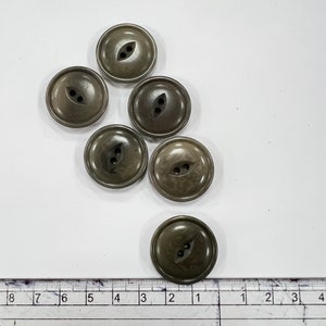 May include: Six olive green buttons with two holes each. The buttons are round with a slightly textured surface. A ruler is visible at the bottom of the image, showing measurements in inches.