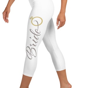 May include: White cropped leggings with the word "Bride" and a gold ring with a diamond graphic on the left leg.