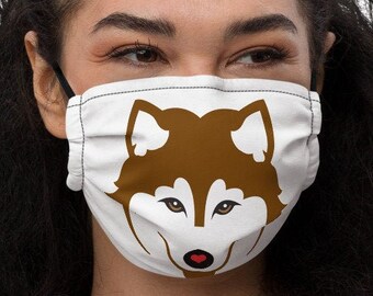 Può includere: Una maschera facciale bianca con un design a forma di muso di husky marrone e bianco. Il cane ha il naso rosso.
