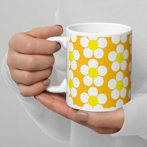 May include: White ceramic mug with a yellow background and a white daisy pattern. The daisies have yellow centers.
