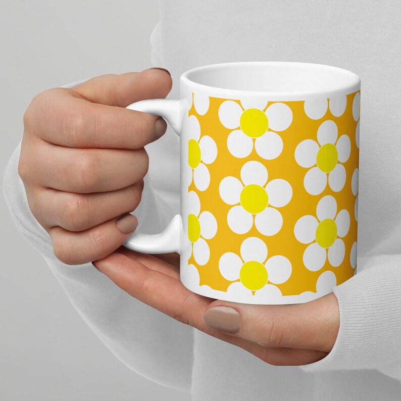 May include: White ceramic mug with a yellow background and a white daisy pattern. The daisies have yellow centers.