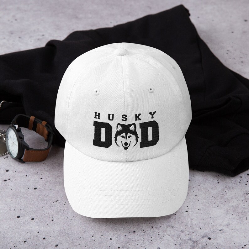 May include: White baseball cap with black embroidery that reads "Husky Dad" with a husky dog silhouette in the middle of the word "Dad".